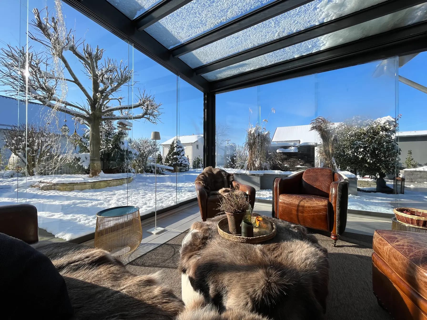 Schneebedecktes Glasdach einer verglasten Terrassenüberdachung von innen, dahinter der verschneite Garten