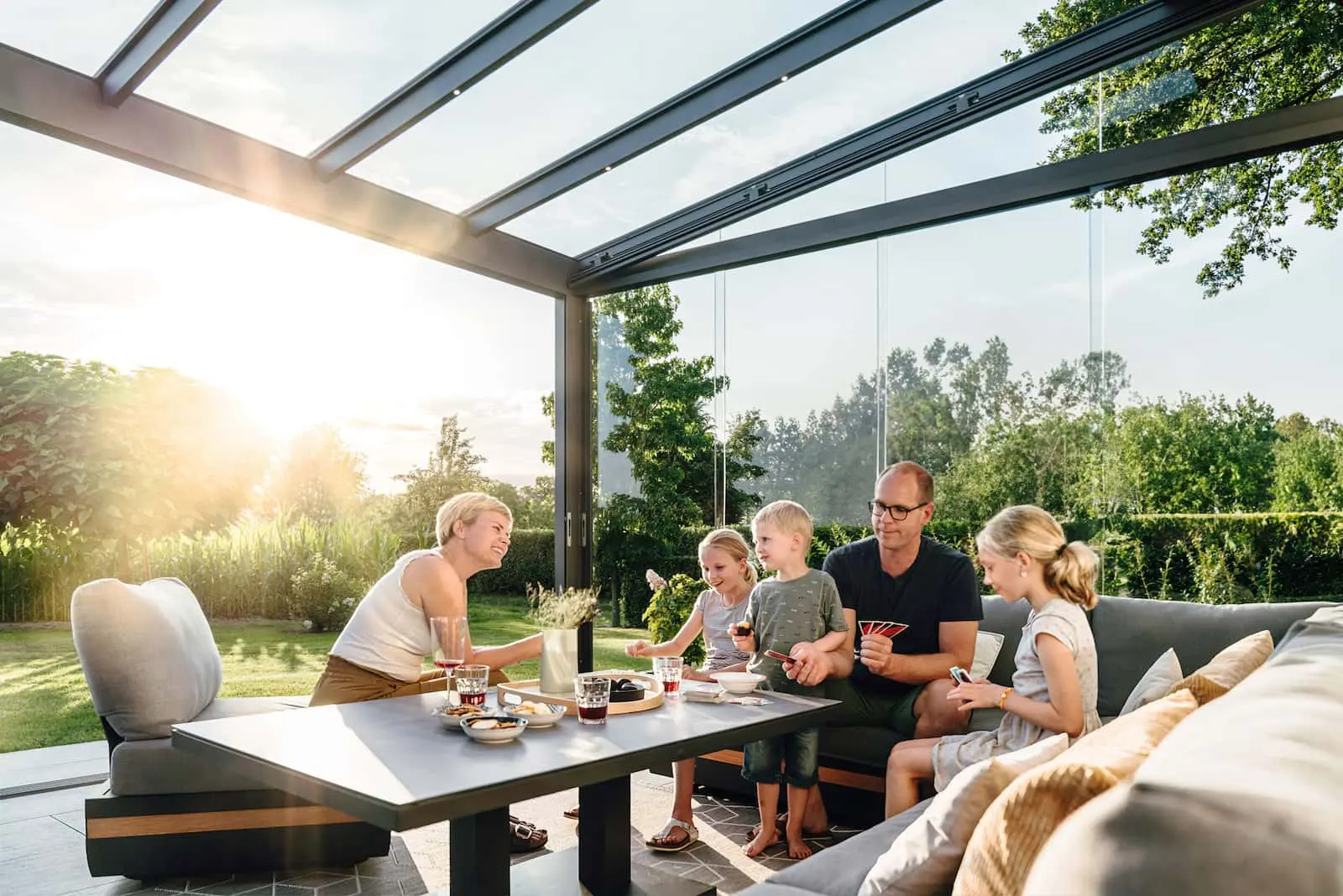 Familie sitzt bei tiefstehender Abendsonne in einem verglasten Wintergarten