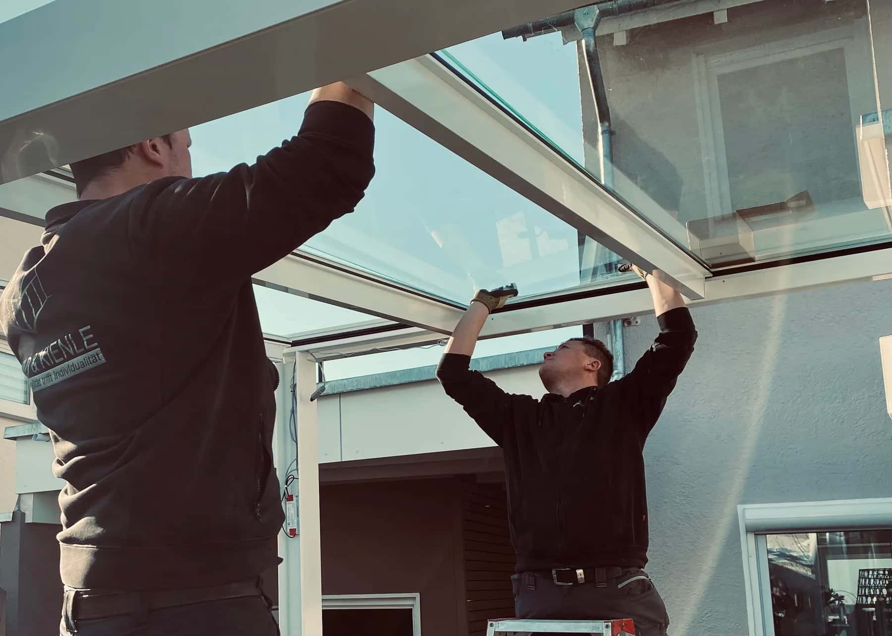 Zwei Monteure setzen ein Glaselement in eine Terrassenüberdachung ein