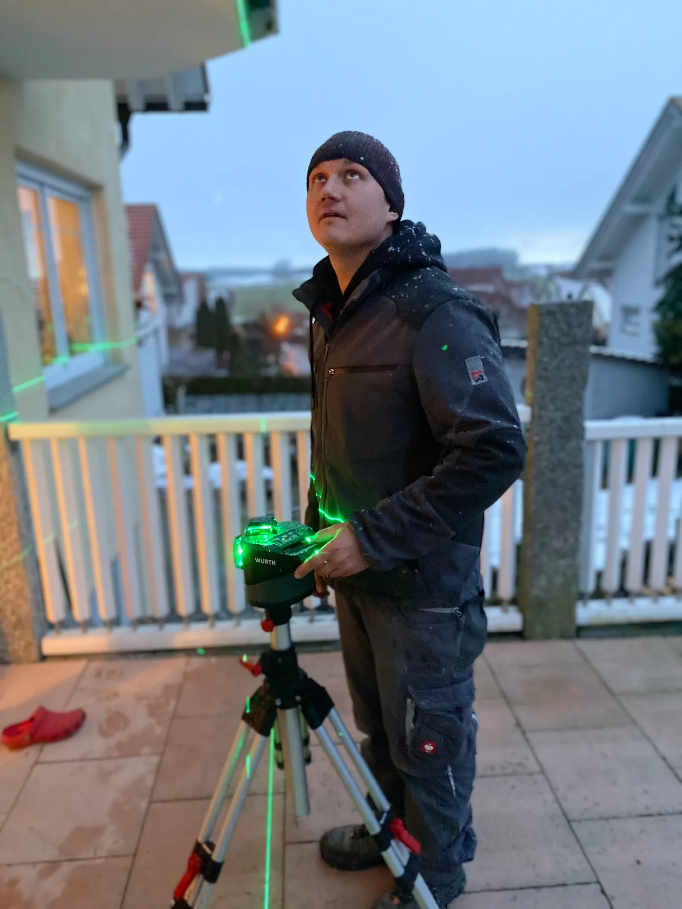 Monteur richtet bei Schneefall den Laser für eine Terrassenüberdachung aus
