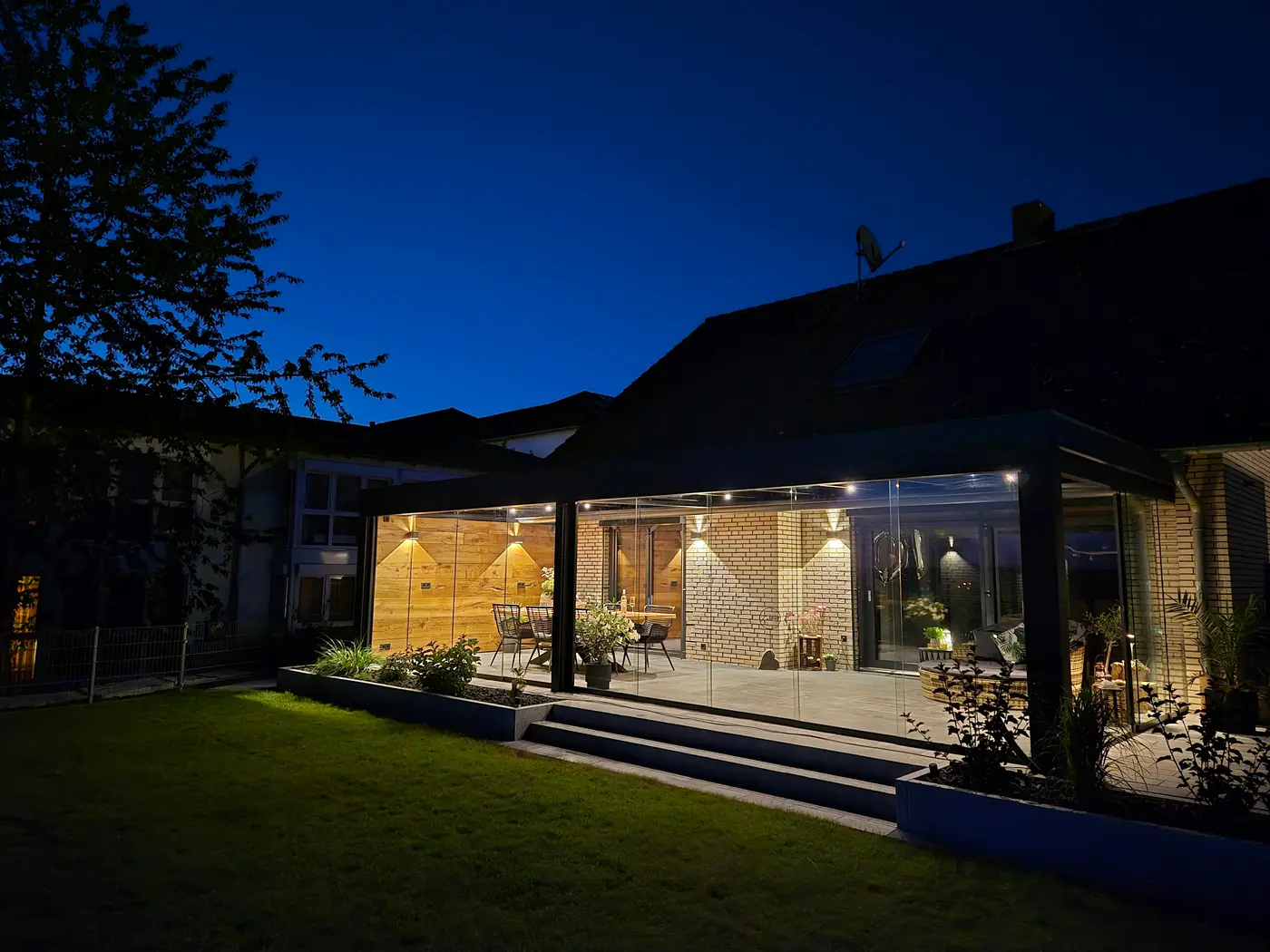 Verglaster Anbau am späten Abend, in die Profile integrierte LED-Spots beleuchten Sitzplatz und Wand