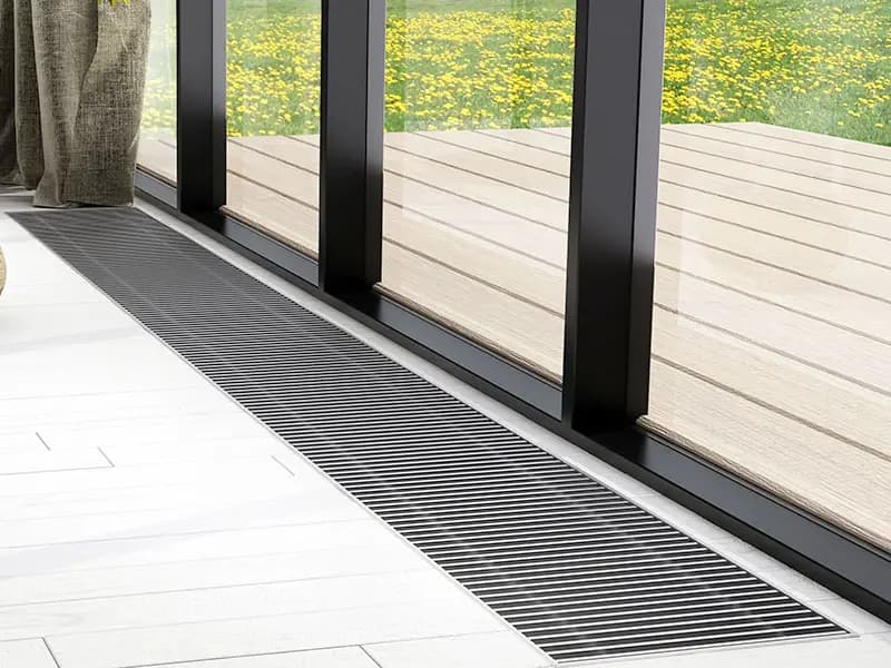 Unterflurkonvektor als schmales Gitter im Boden entlang der Glasfront, dahinter die Terrasse