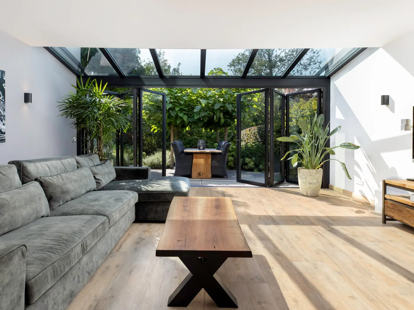 Wohn-Wintergarten mit weit geöffneter Glas-Faltwand, davor die Terrasse und der Garten, innen Sofa und Couchtisch