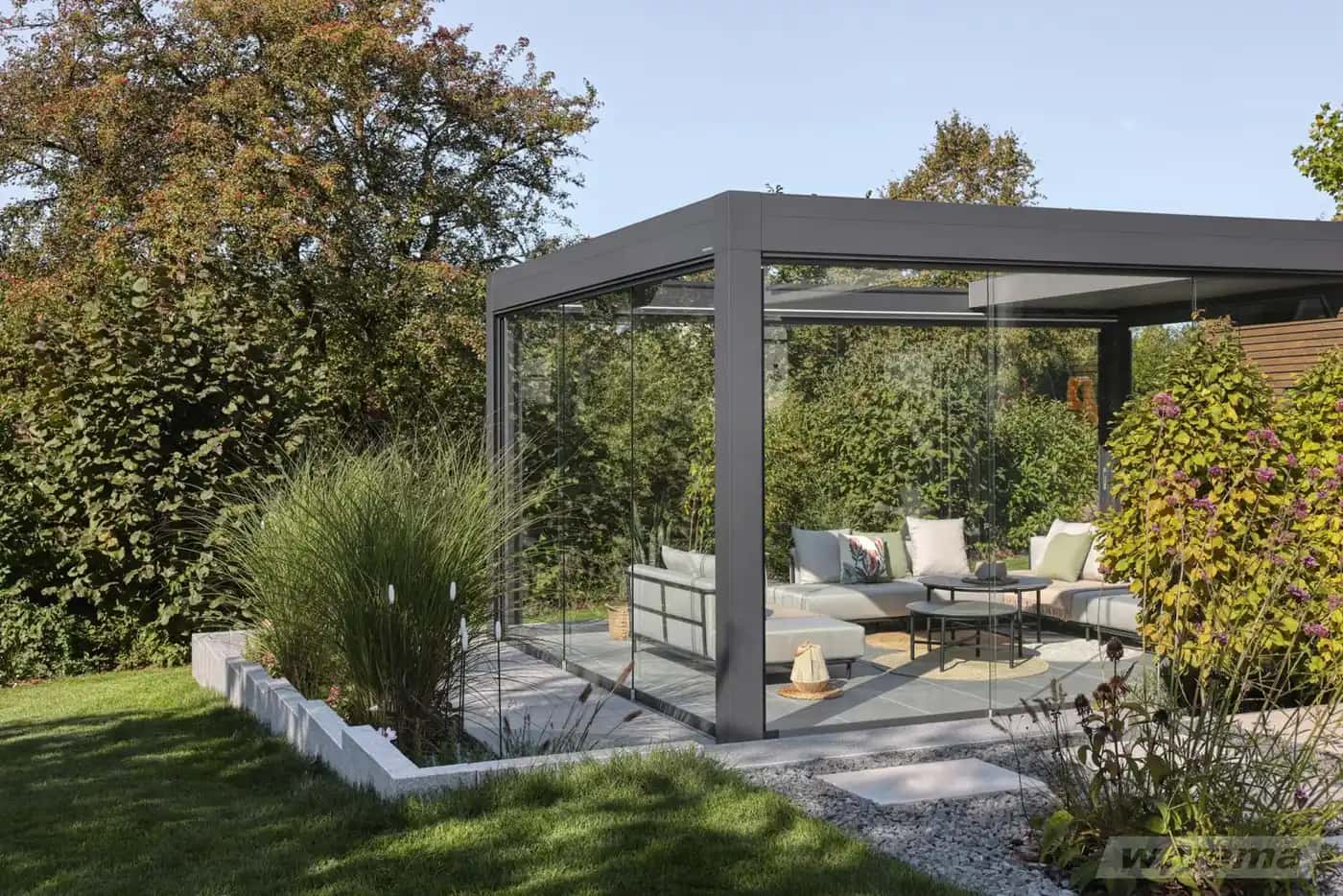 Freistehendes Warema Lamaxa L70 Lamellendach mit geöffneten Lamellen und seitlichen Glasschiebewänden über einer Garten-Lounge