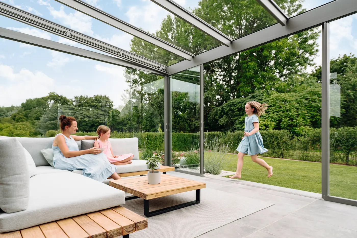 Als Kaltwintergarten verglastes Terrassendach mit geöffneten Glas-Schiebeelementen, Lounge-Möbel im Trockenen, der Garten direkt davor