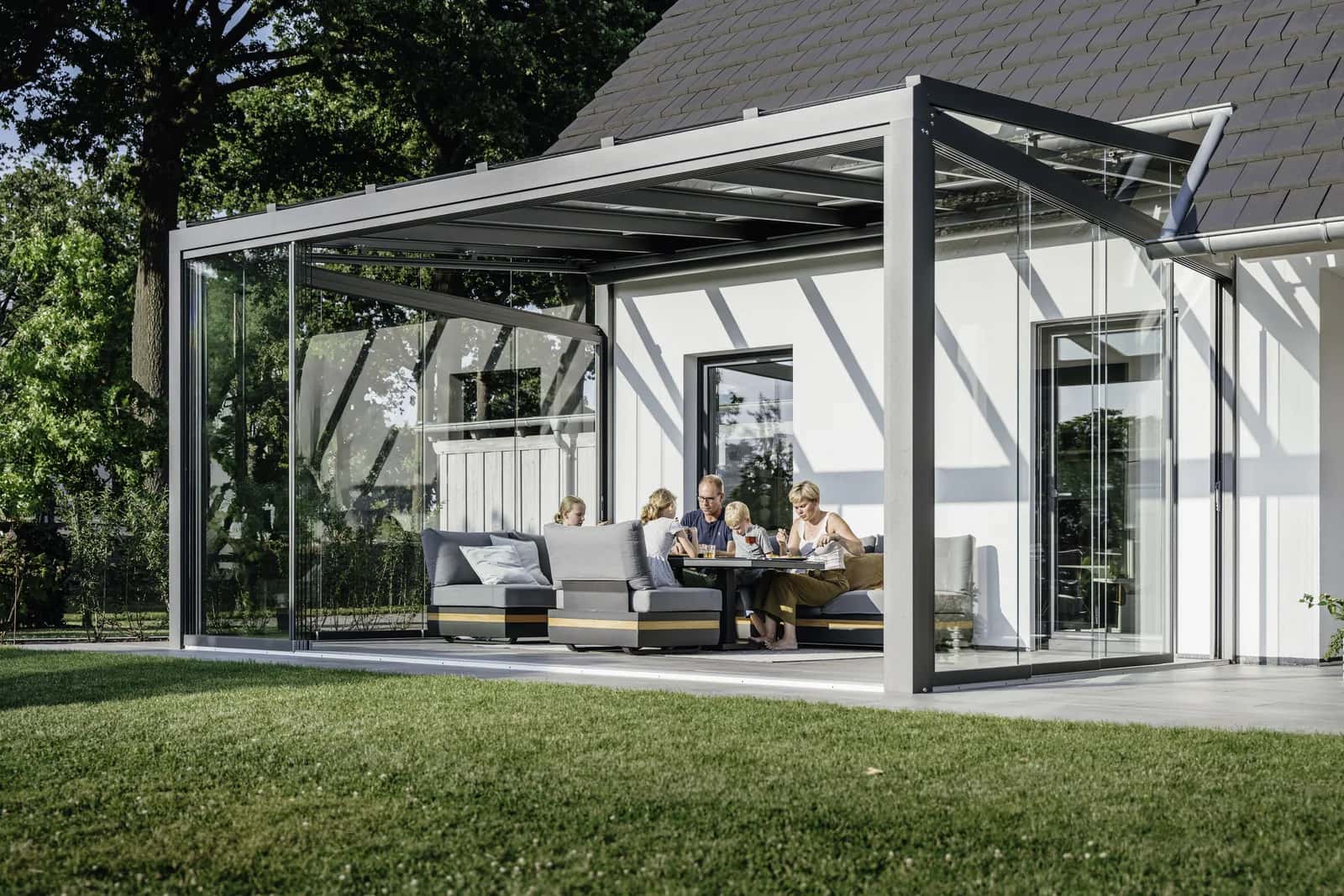 Familie am Esstisch unter dem filigranen Solarlux SDL Alerio Terrassendach mit geöffneten Glas-Schiebewänden