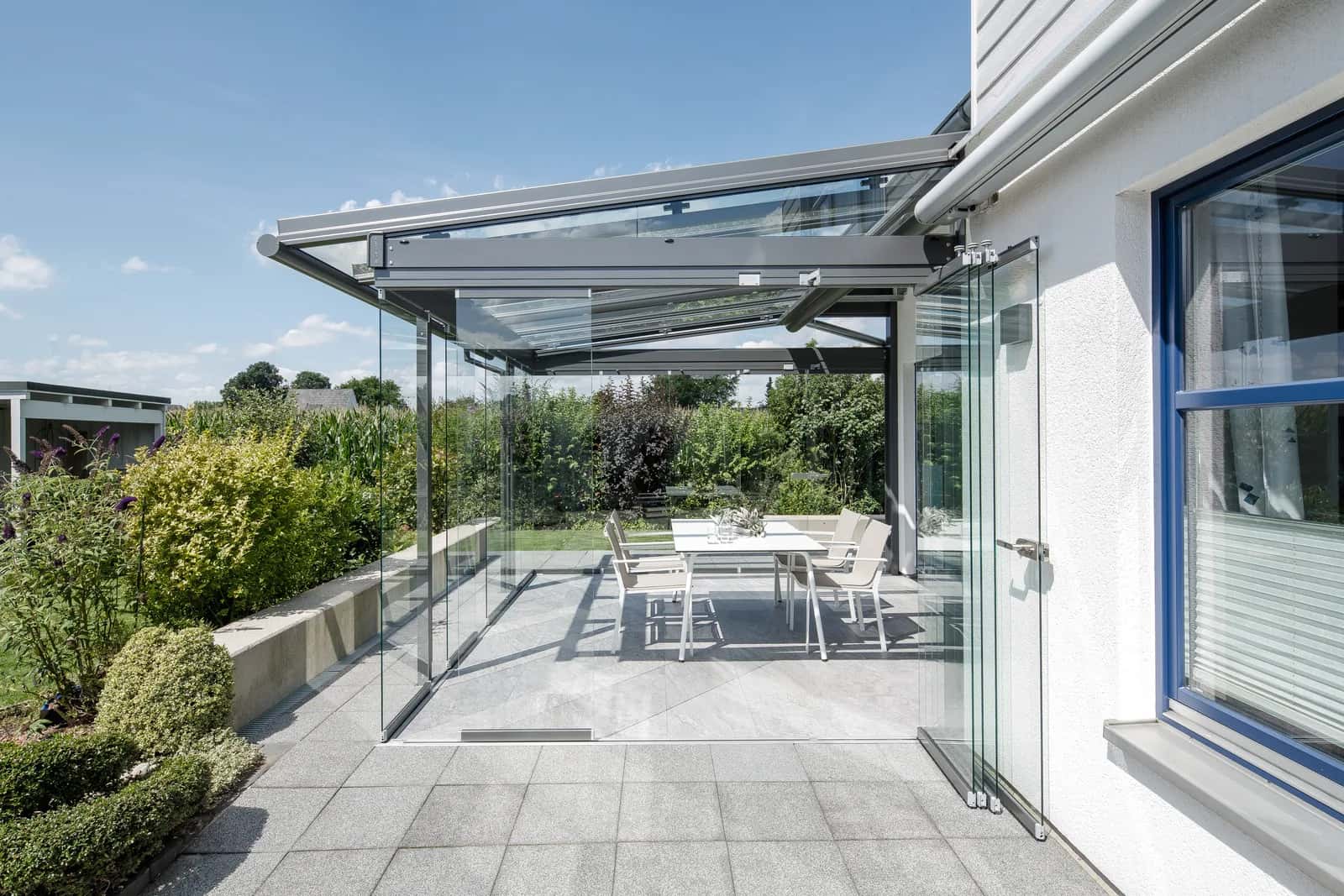Solarlux SDL Atrium Plus Terrassendach mit Glasdach und geöffneter Glas-Faltwand an einem weißen Wohnhaus