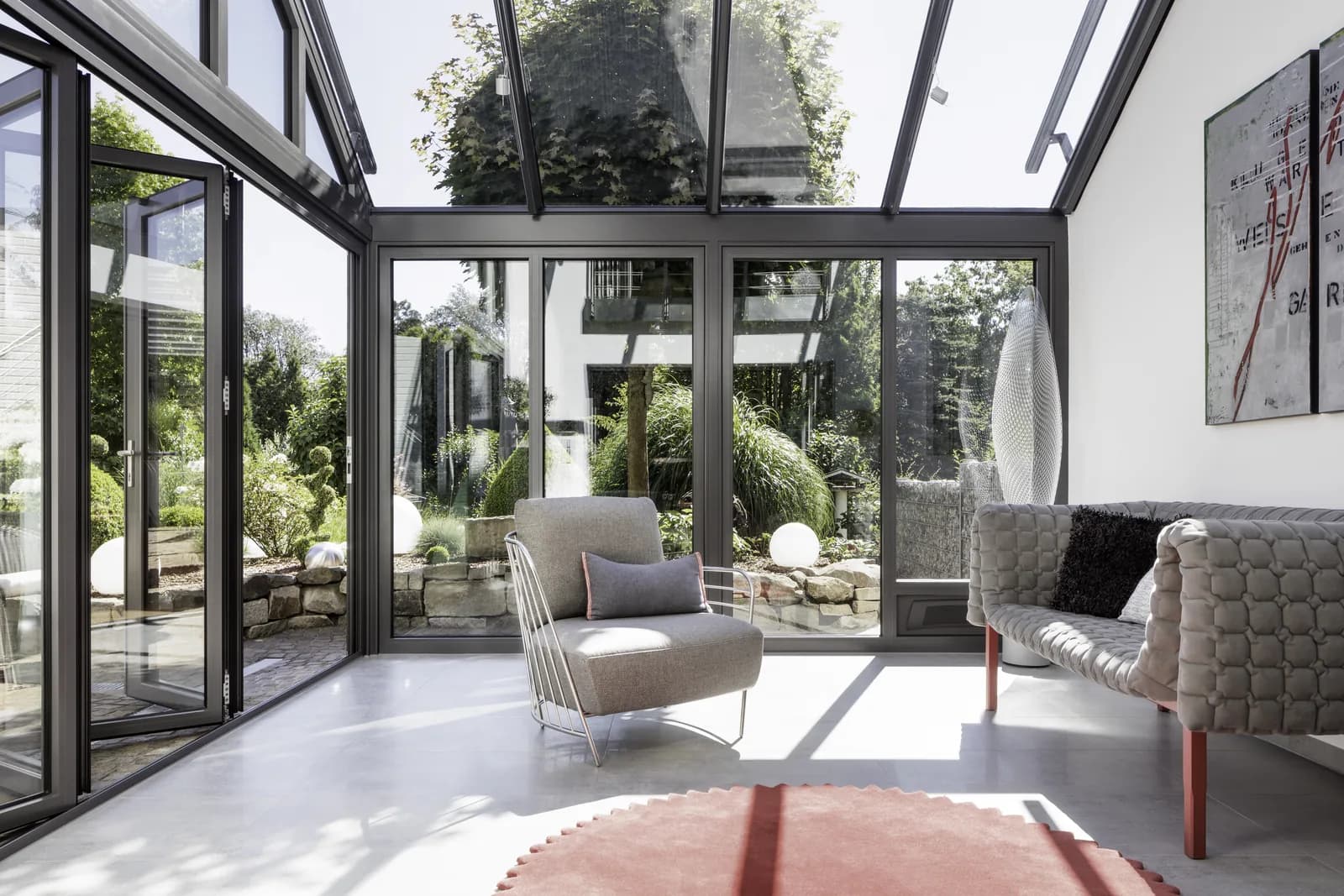 Sonniger Innenblick in den SDL Nobiles Wintergarten mit schlanken Design-Sparren, Glas-Faltwand und Gartenblick