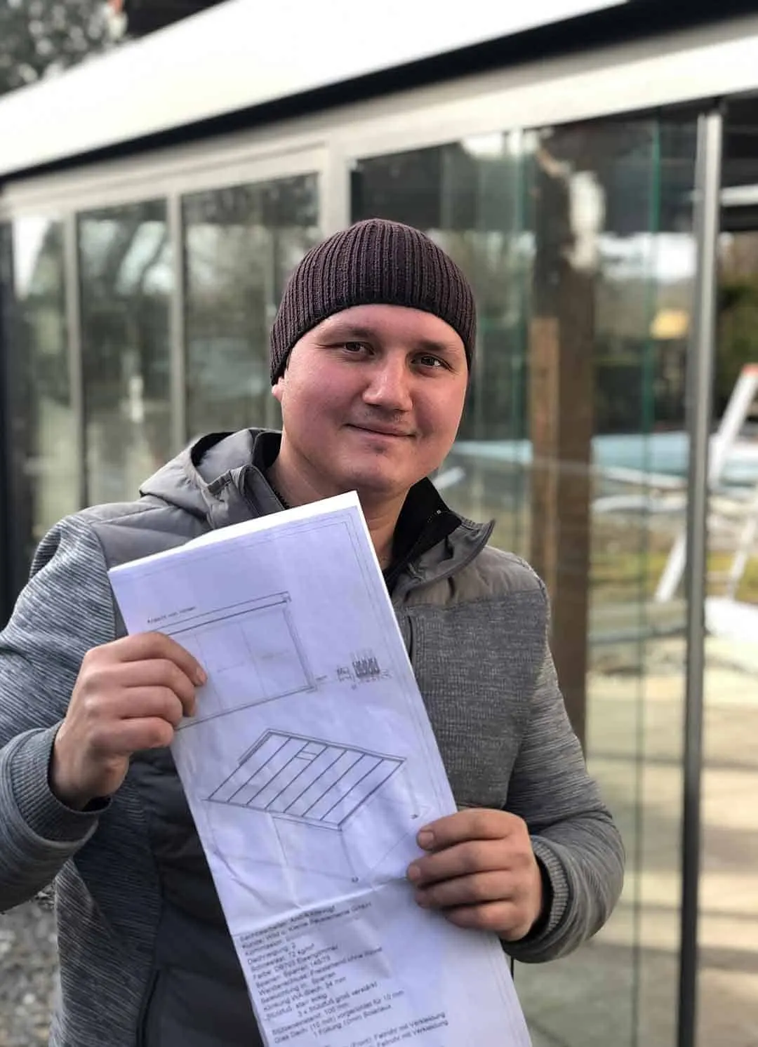 Monteur von Wild & Kienle mit Montageplan vor einer verglasten Terrassenüberdachung