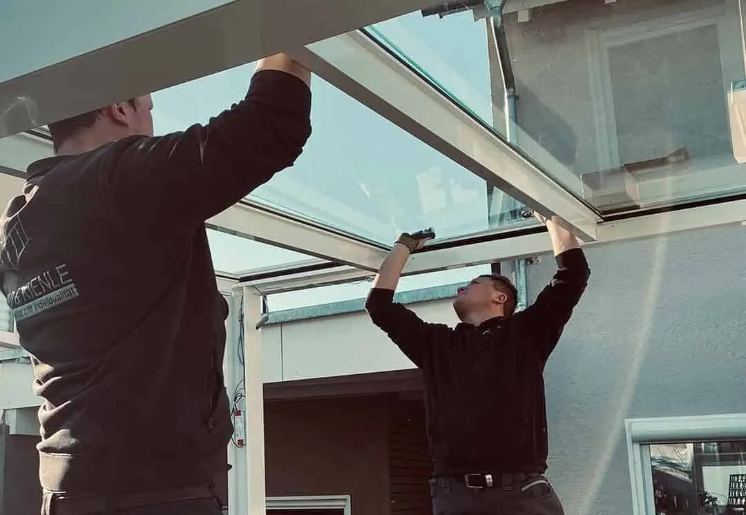 Zwei Monteure setzen eine Glasscheibe in das Dach einer Terrassenüberdachung ein