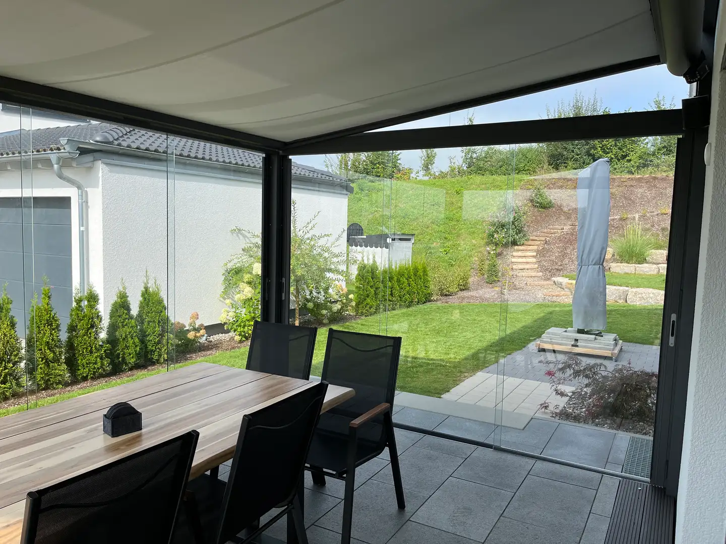 Blick aus dem Glashaus mit Glas-Schiebewänden und ausgefahrener Unterglasmarkise in den Garten im Raum Bad Saulgau
