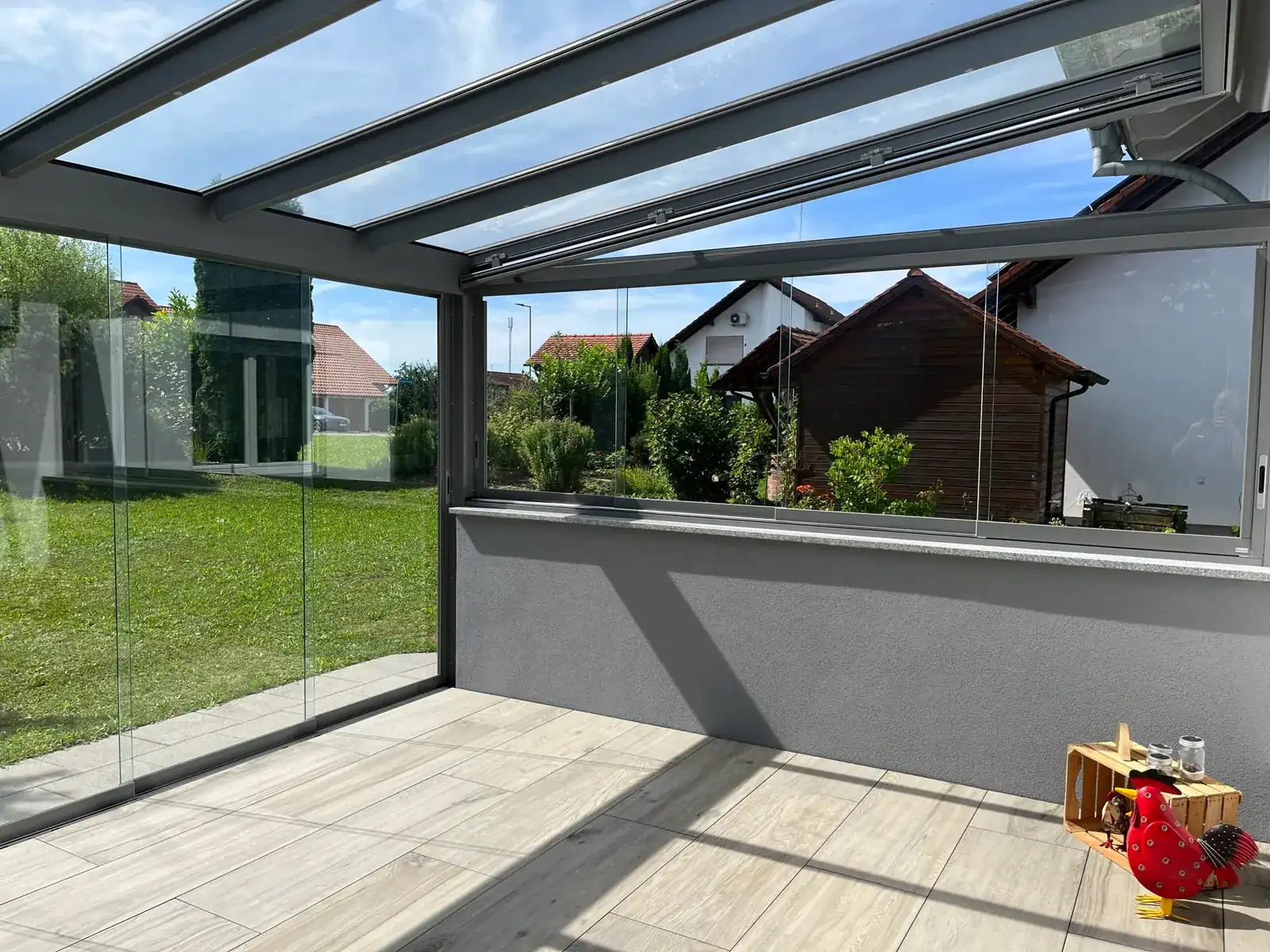 Innen im Kaltwintergarten: über der grauen Brüstungsmauer sitzen Schiebefenster