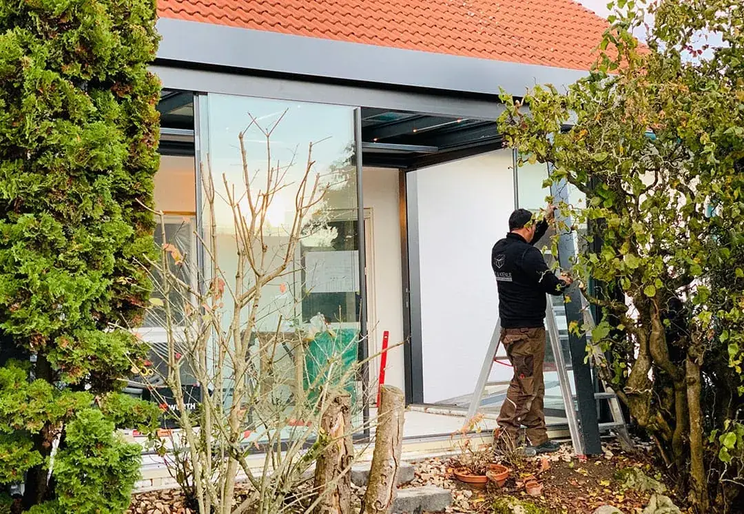 Montage der Glas-Schiebeelemente: ein Monteur arbeitet auf der Leiter an der Ecke des Kaltwintergartens