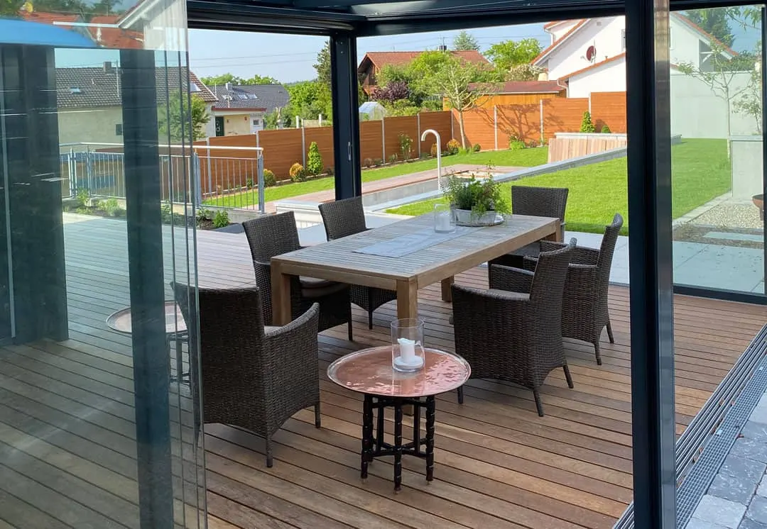 Blick vom Esstisch über das Geländer in den tiefer liegenden Garten mit Rasen und Wasserbecken