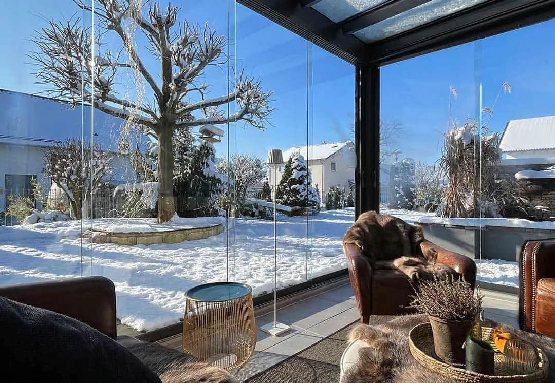 Ganzglas-Schiebewände mit Blick auf den verschneiten Baum, davor Ledersessel mit Fellen