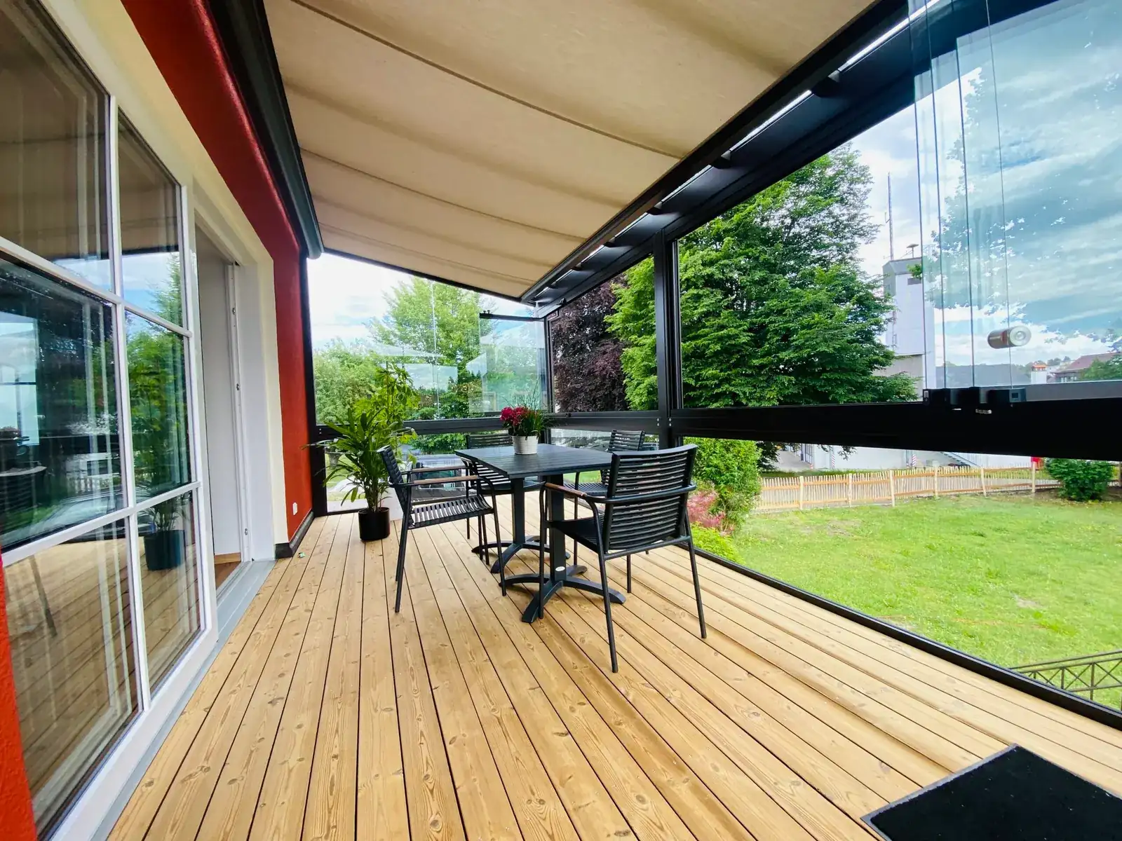 Der Kaltwintergarten an der roten Hauswand entlang, die Glasscheiben geöffnet zur Seite geschoben