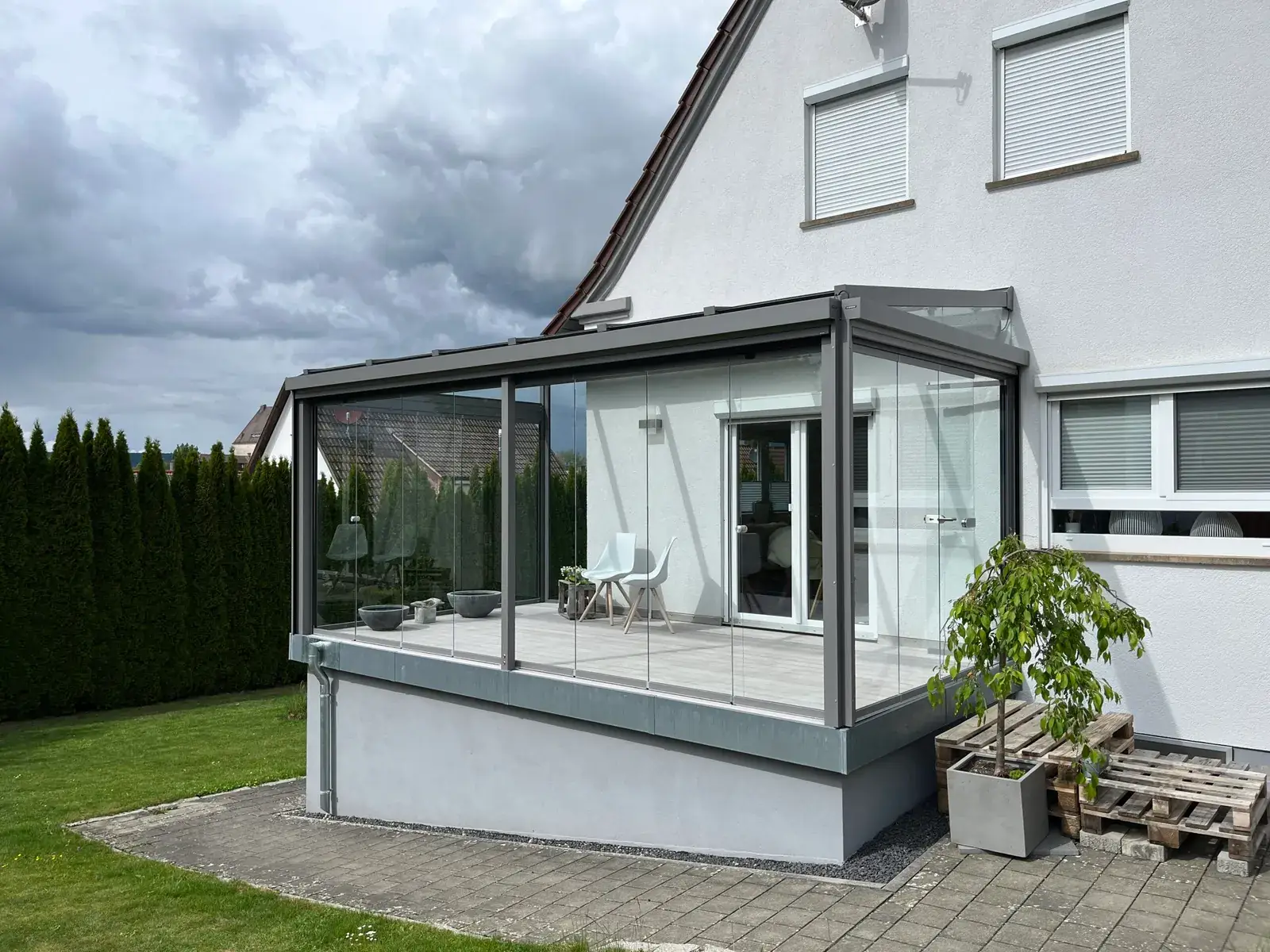 Der Kaltwintergarten von der Gartenseite: Glaselemente auf der Kante des verputzten Sockels, dahinter die weiße Fassade mit der Terrassentür