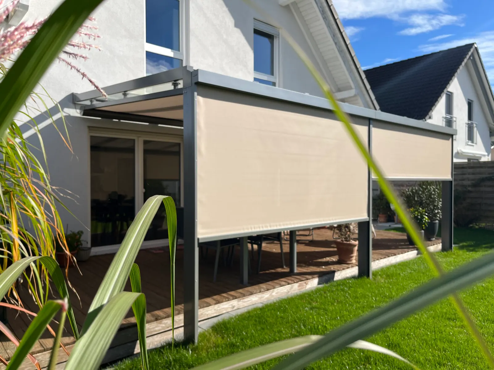 Zwei beige Senkrechtmarkisen sind an der Gartenseite heruntergefahren, dahinter liegt die Sitzgruppe im Schatten