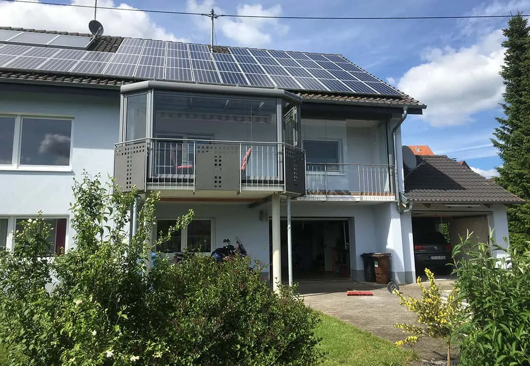 Der verglaste Balkon nach dem Umbau: unter dem neuen Glasdach ist die gestreifte Markise ausgefahren, auf dem Hausdach liegt die Photovoltaikanlage