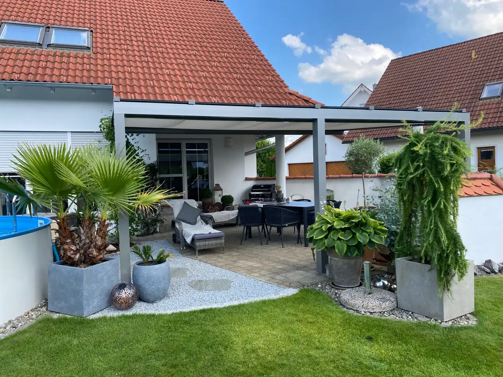 Haus und Terrassendach vom Garten aus, unter dem Glasdach ist die Markise ausgefahren