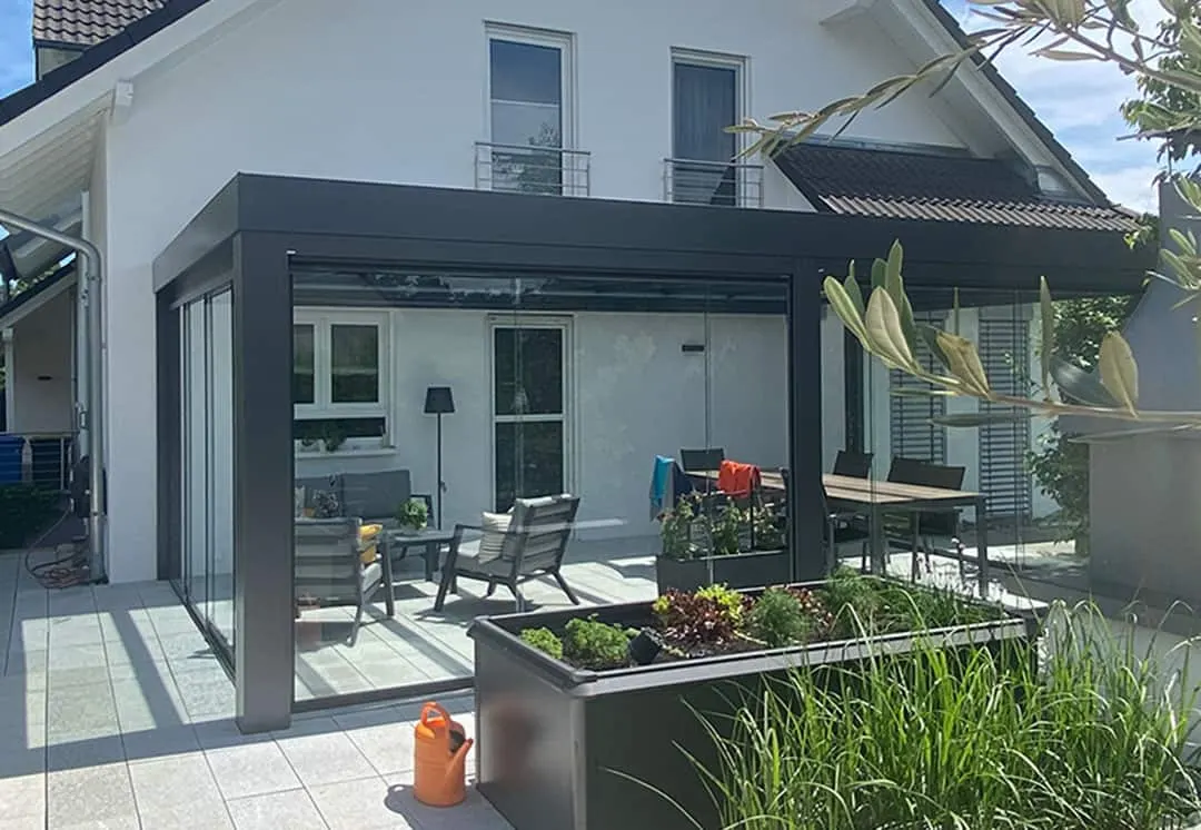 Das Terrassendach vom Garten aus, davor das Hochbeet mit Salat und Kräutern und eine orange Gießkanne