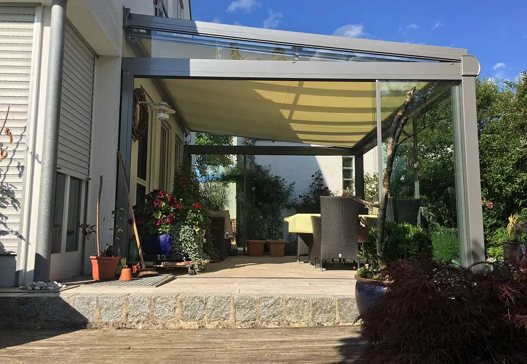 Die Überdachung an der Kante der erhöhten Terrasse, unter dem Glasdach ist die helle Markise komplett ausgefahren