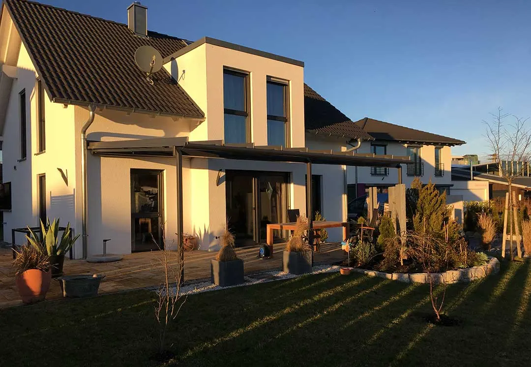 Blick über den Rasen auf das Terrassendach vor den beiden Baukörpern des Wohnhauses