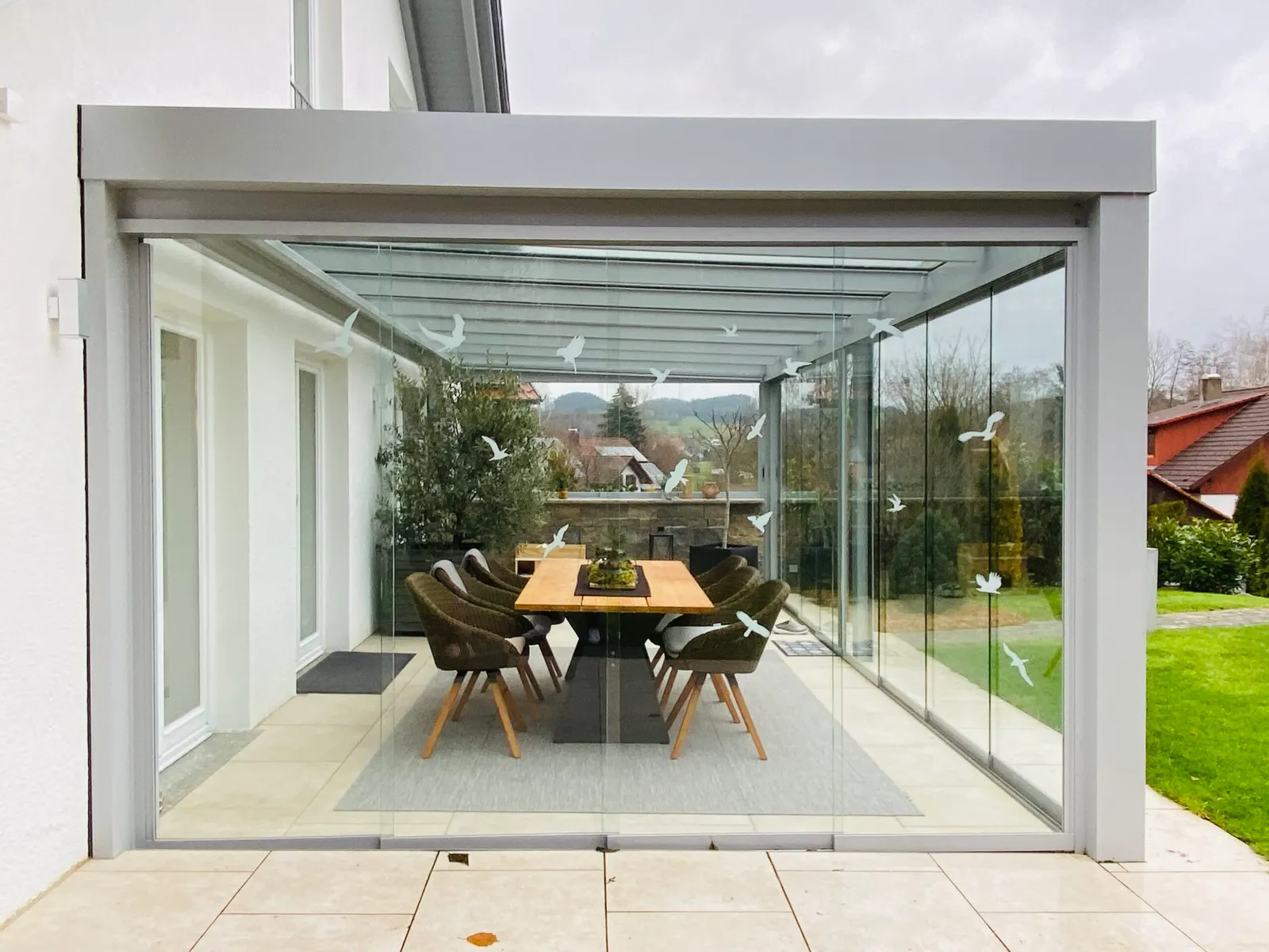 Die geschlossene Glasfront von außen, dahinter der lange Holztisch mit dem Moosgesteck