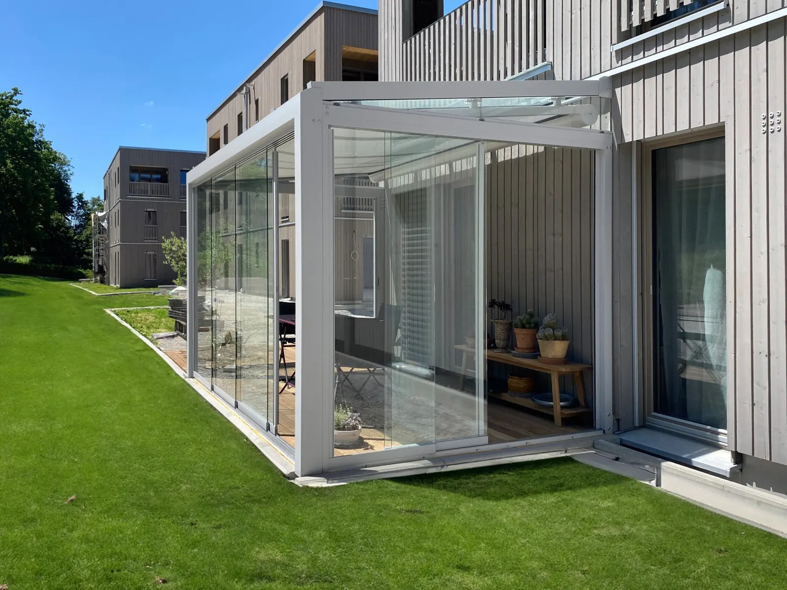 Die geöffneten Glasschiebeelemente an der Ecke des Glashauses, dahinter die Terrassentür der Wohnung