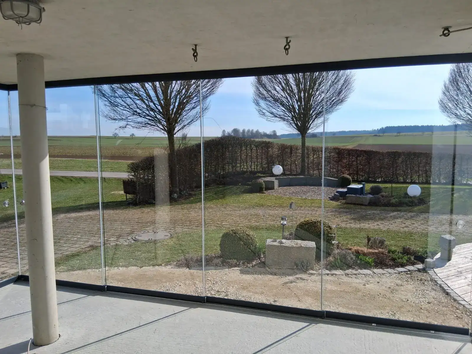 Blick aus dem verglasten Freisitz über den Garten auf Hecken und Felder