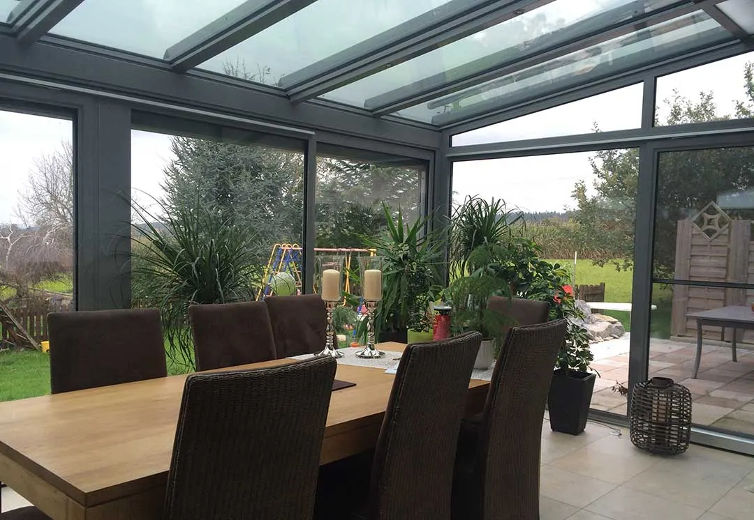Blick aus dem Wintergarten in den Garten mit Schaukel und Klettergerüst, im Vordergrund der Esstisch mit Kerzenleuchtern