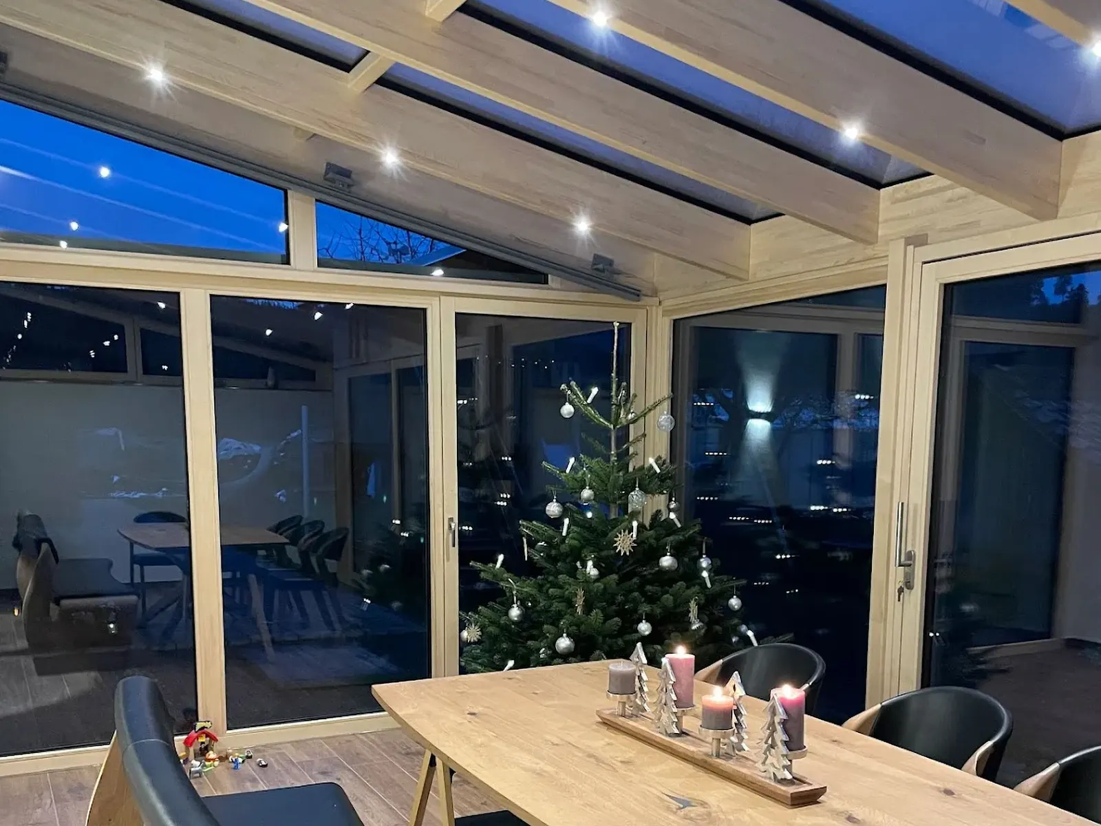 Innenansicht mit LED-Spots in den hellen Leimholzsparren, davor Esstisch mit Adventsgesteck und Christbaum