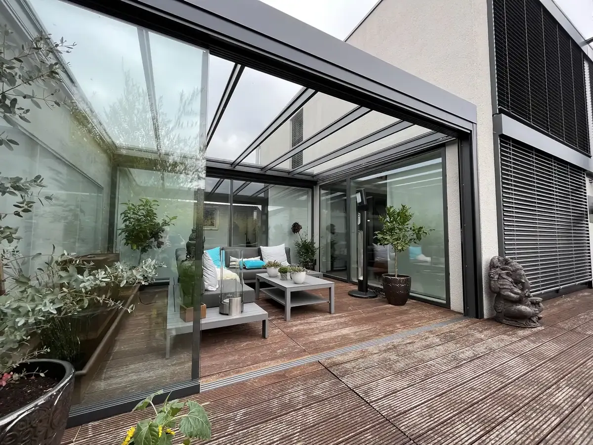 Die geschlossene Glasfront zwischen Hauswand und Betonmauer, in den Scheiben spiegelt sich der Garten