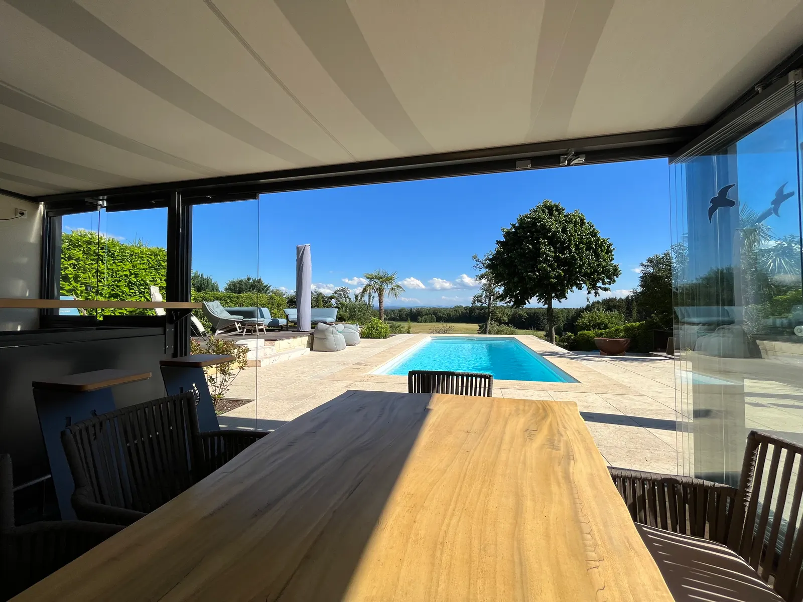 Blick unter dem Glasdach hinaus auf Pool und offenes Land