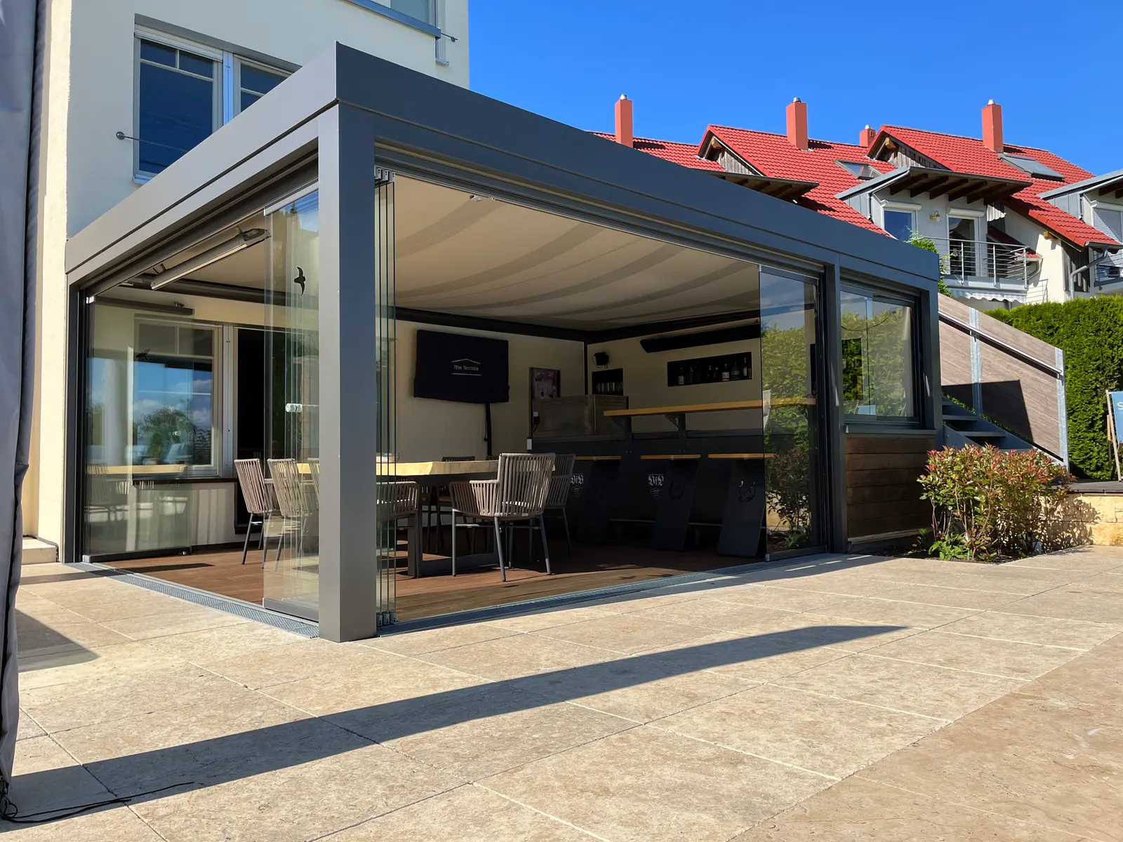 Blick durch die offene Ecke auf Bar, Esstisch und Fernseher unter dem Glasdach