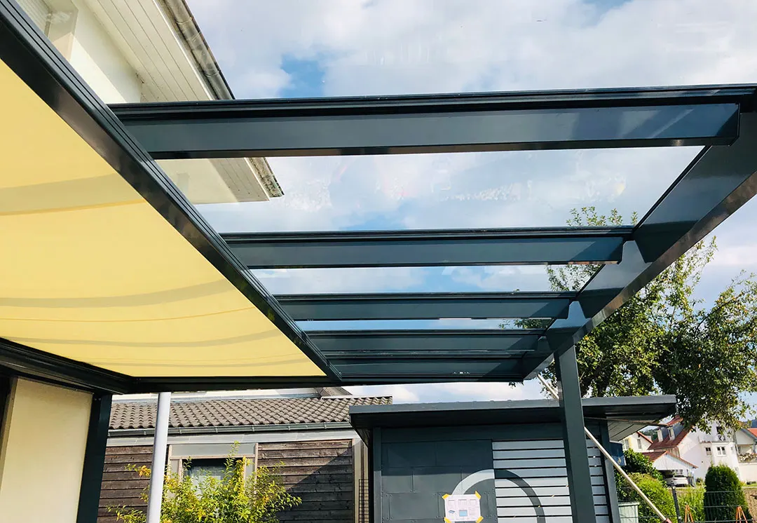 Blick von unten auf die Glasfläche des Terrassendachs, die Unterglasmarkise halb ausgefahren