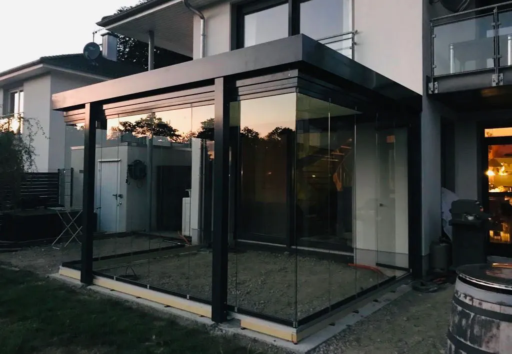 Das Glashaus in der Abenddämmerung, die Glasseiten geschlossen, im Inneren noch der Kies der Baustelle