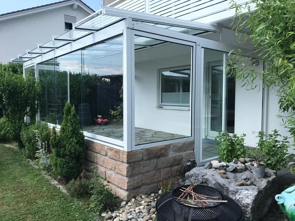 Die Glasfront des Terrassendachs, die unteren Elemente stehen auf der Natursteinmauer