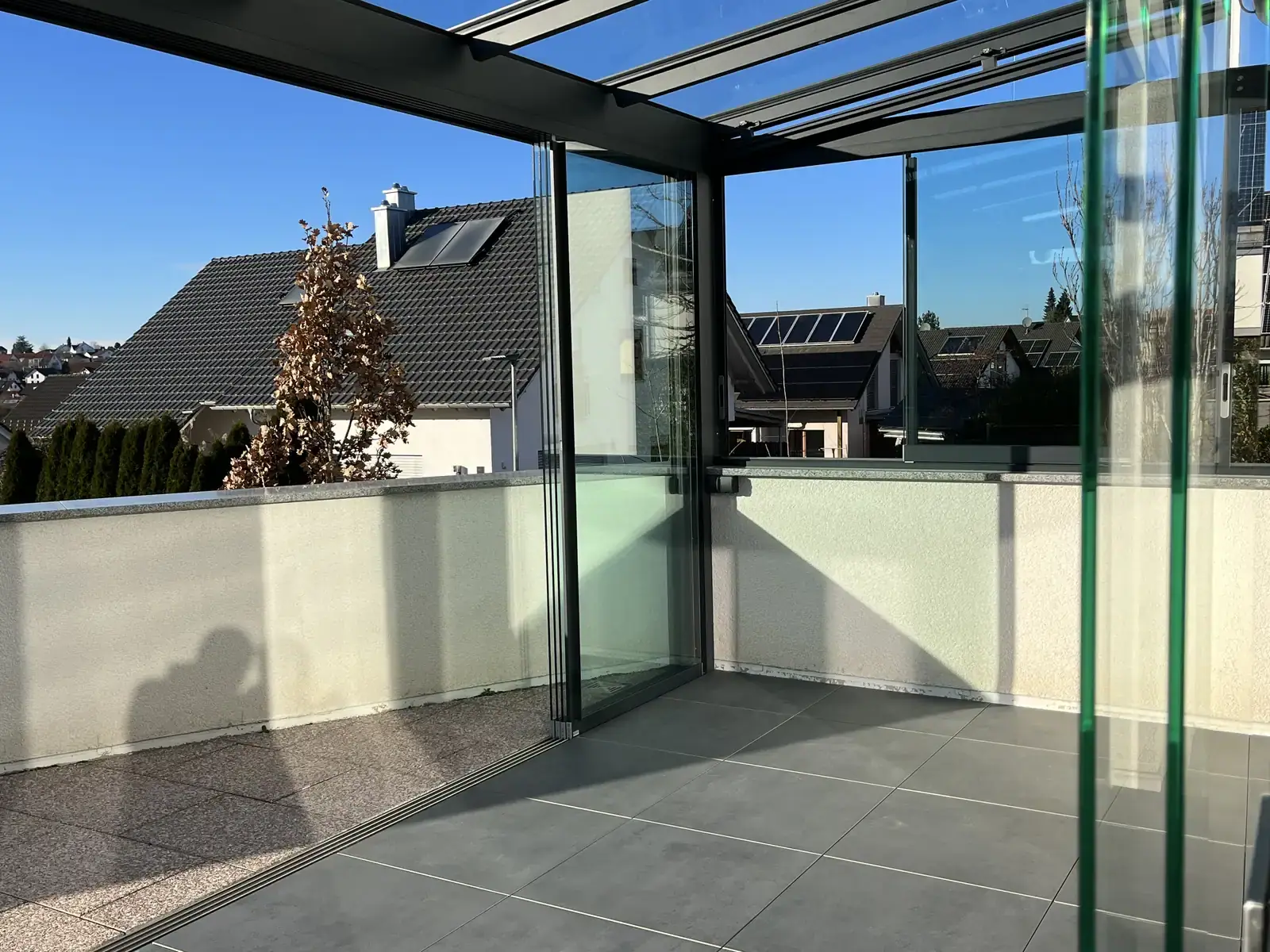 Die niedrigen Schiebefenster sitzen auf der weißen Brüstungsmauer, darüber schließt der feste Glaskeil zum Dach