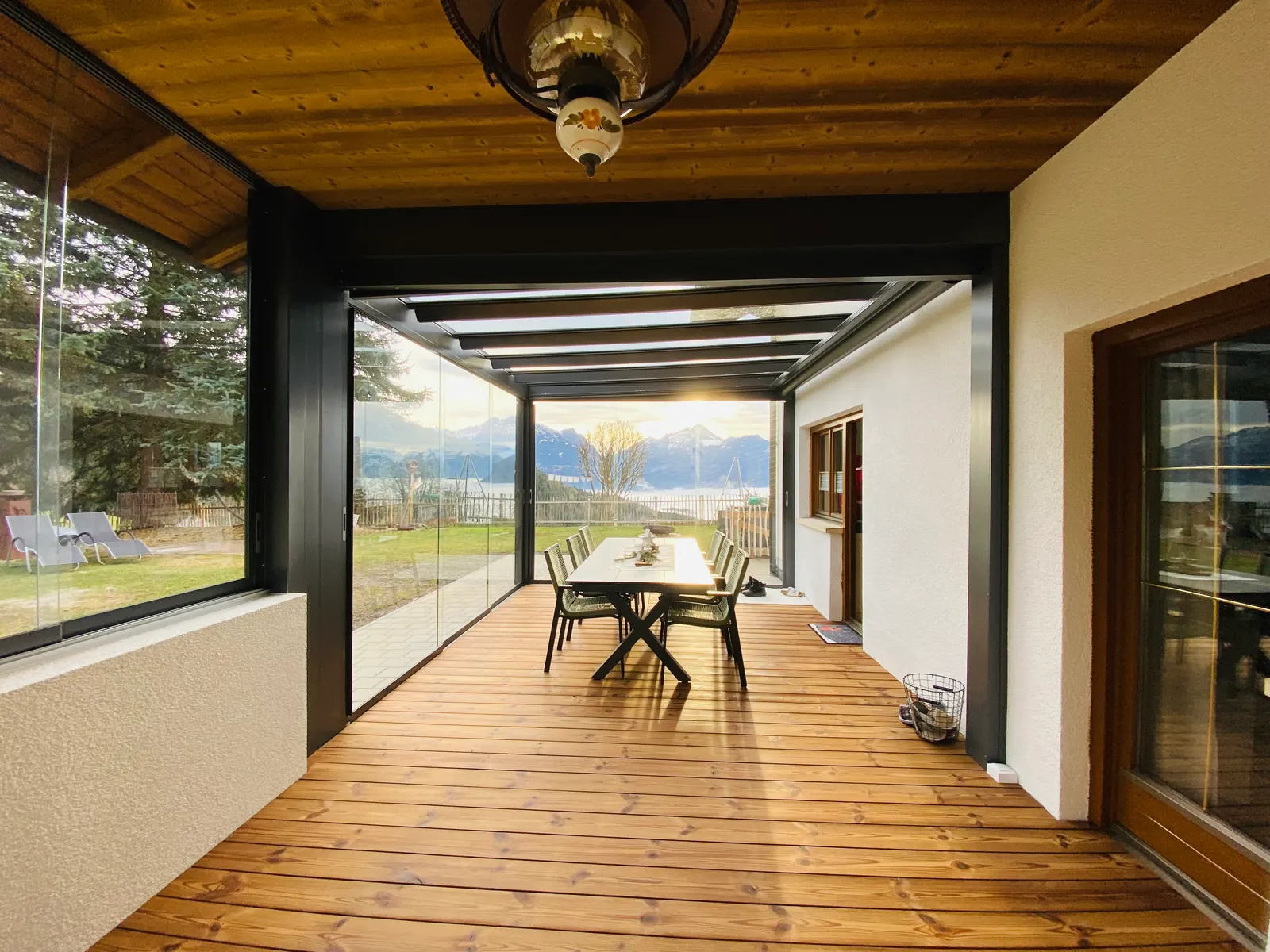 Blick aus der holzgedeckten Loggia durch den neuen Glasanbau auf die Berge