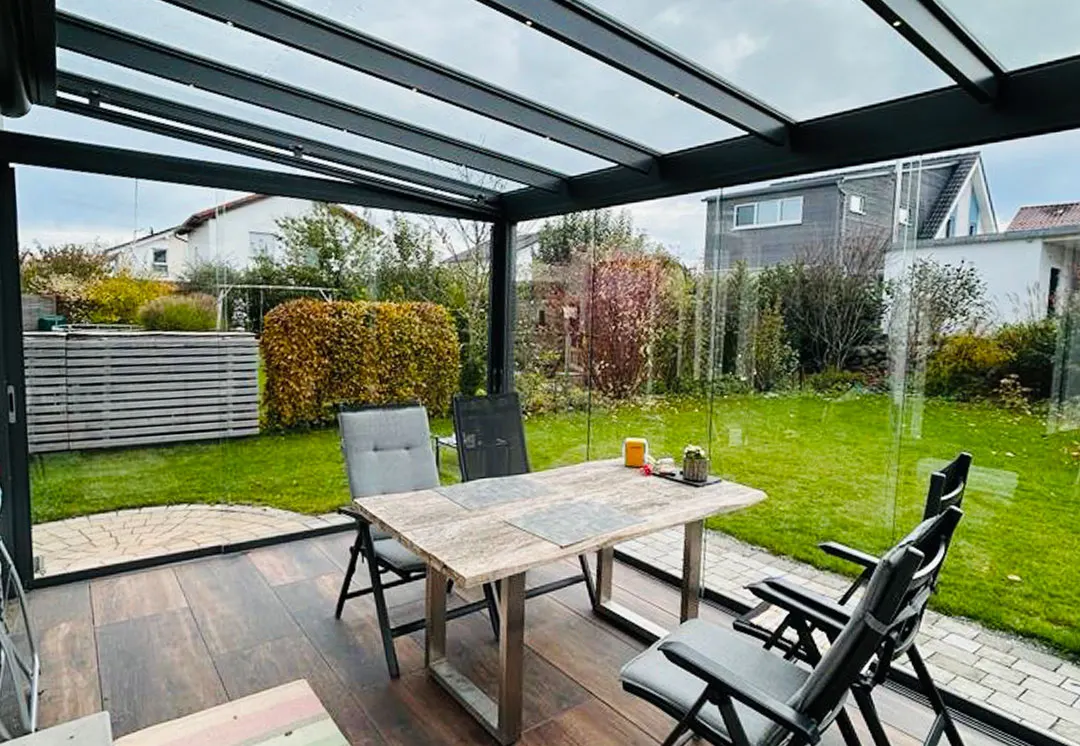 Blick von innen durch die Glasfront in den Garten, davor der Esstisch auf dem Boden in Holzoptik