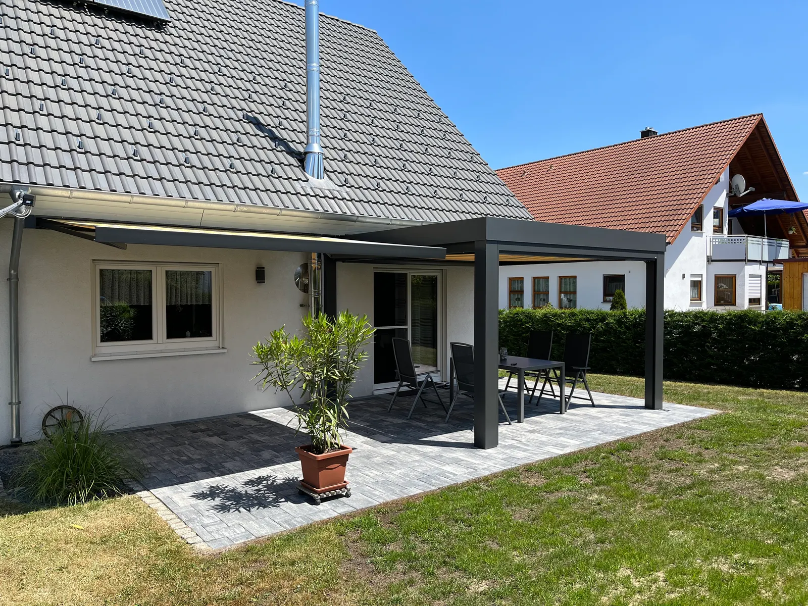 Haus und Terrassendach vom Garten aus, unter dem Glasdach ist die Markise ausgefahren