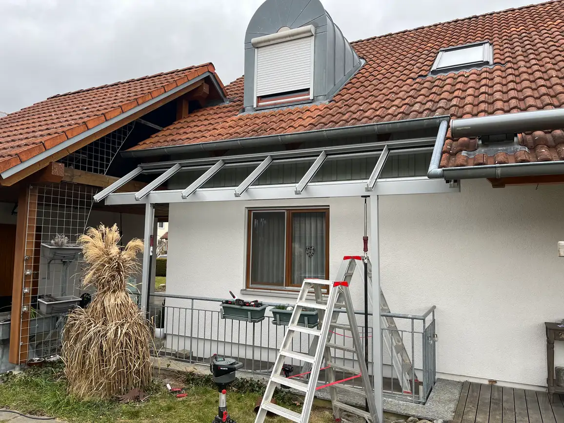 Während der Montage: das Dach sitzt schon unter der Traufe des Hauses, die Leiter lehnt am Geländer des Kellerabgangs