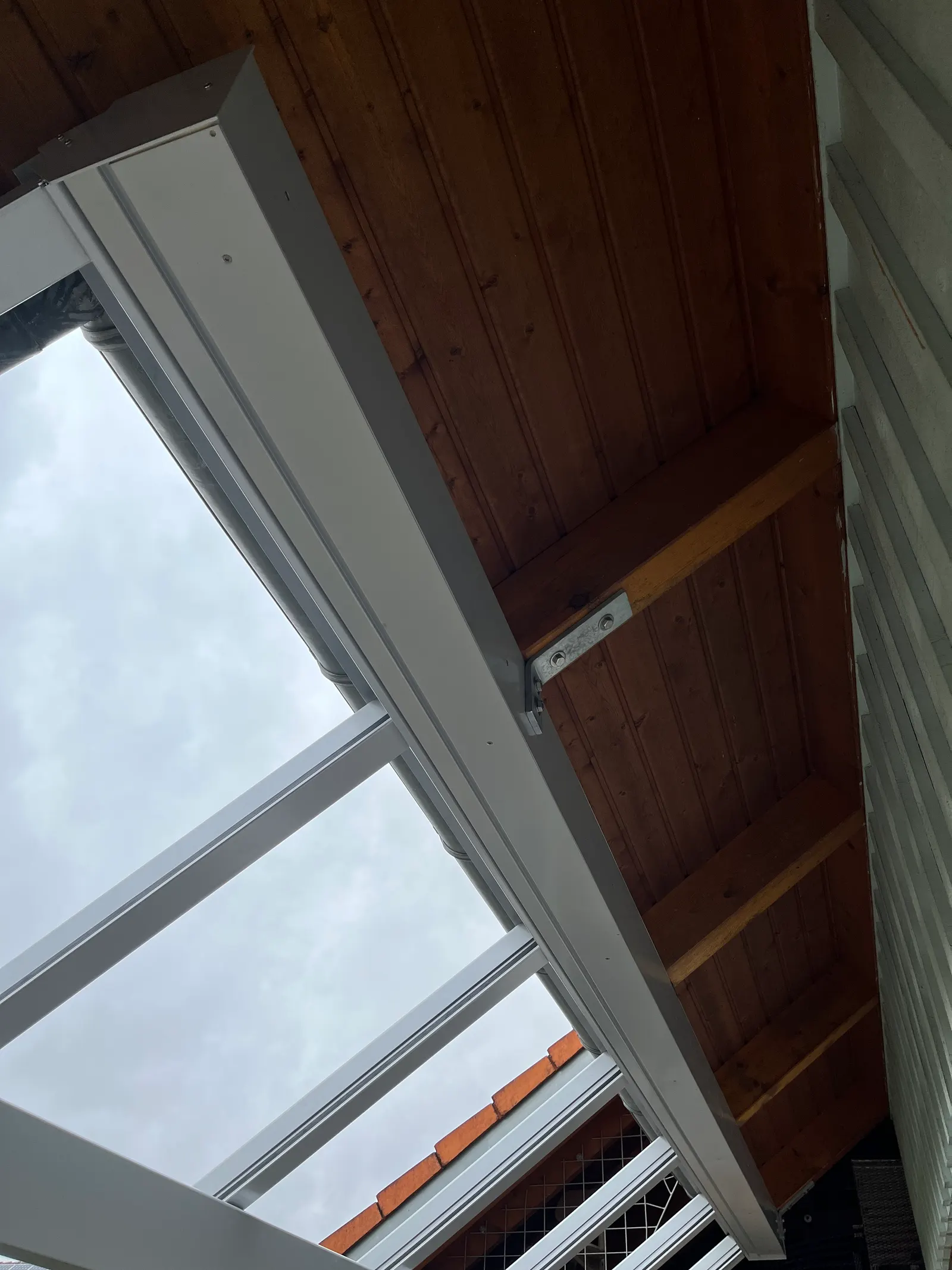 Blick von unten auf den Anschluss: der Stahlwinkel sitzt am Holzsparren des Hausdachs, daran hängt das hintere Profil des Glasdachs